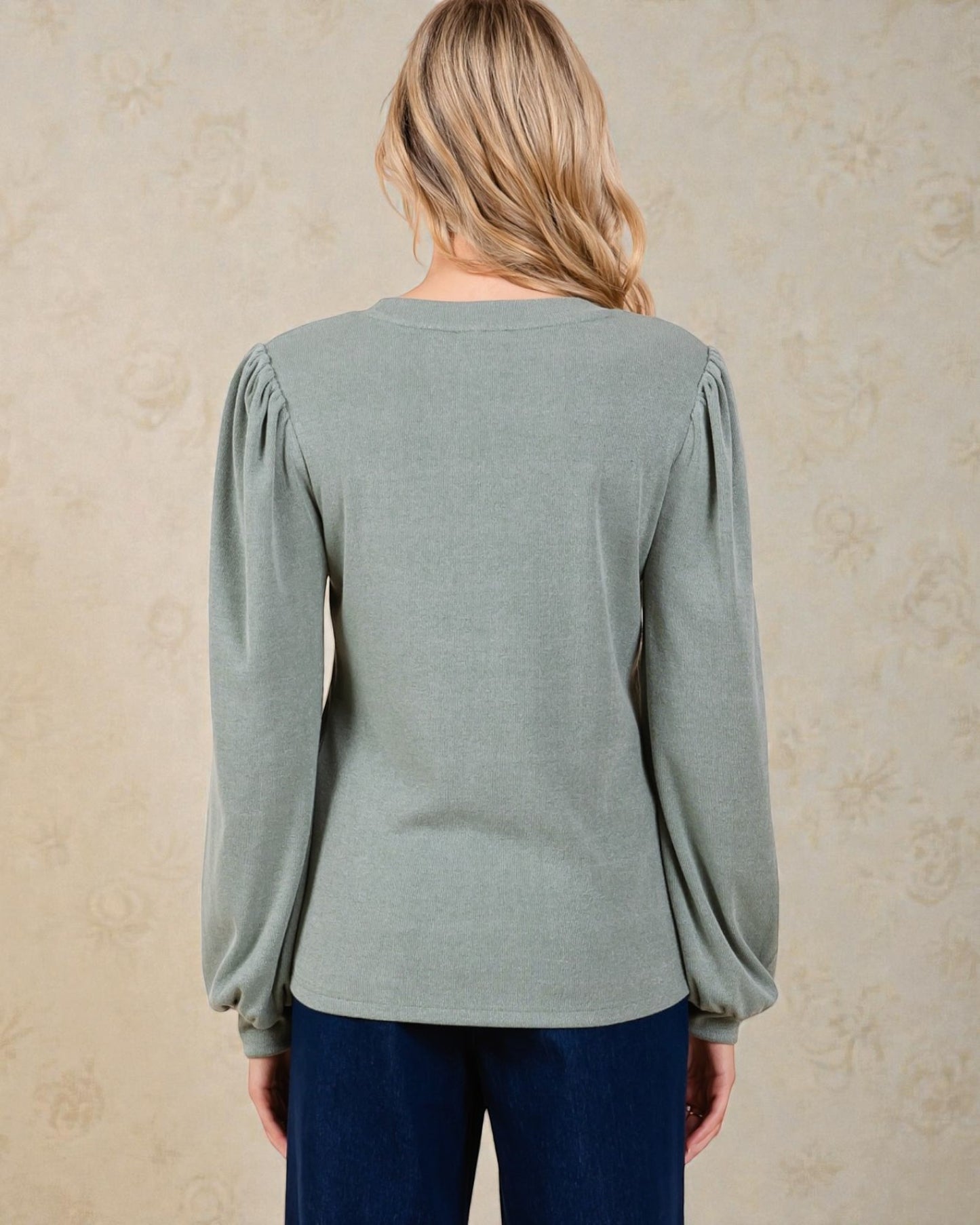 Person wearing a light green long-sleeve top with puffed sleeves against a beige background