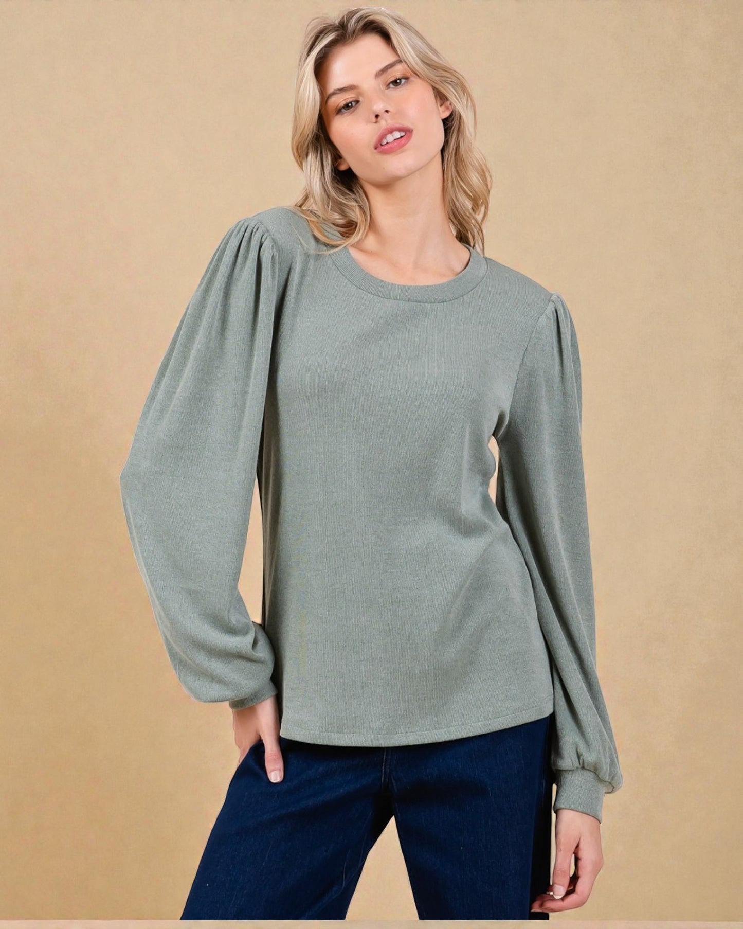 Woman wearing a green sweater with puffed sleeves against a beige background