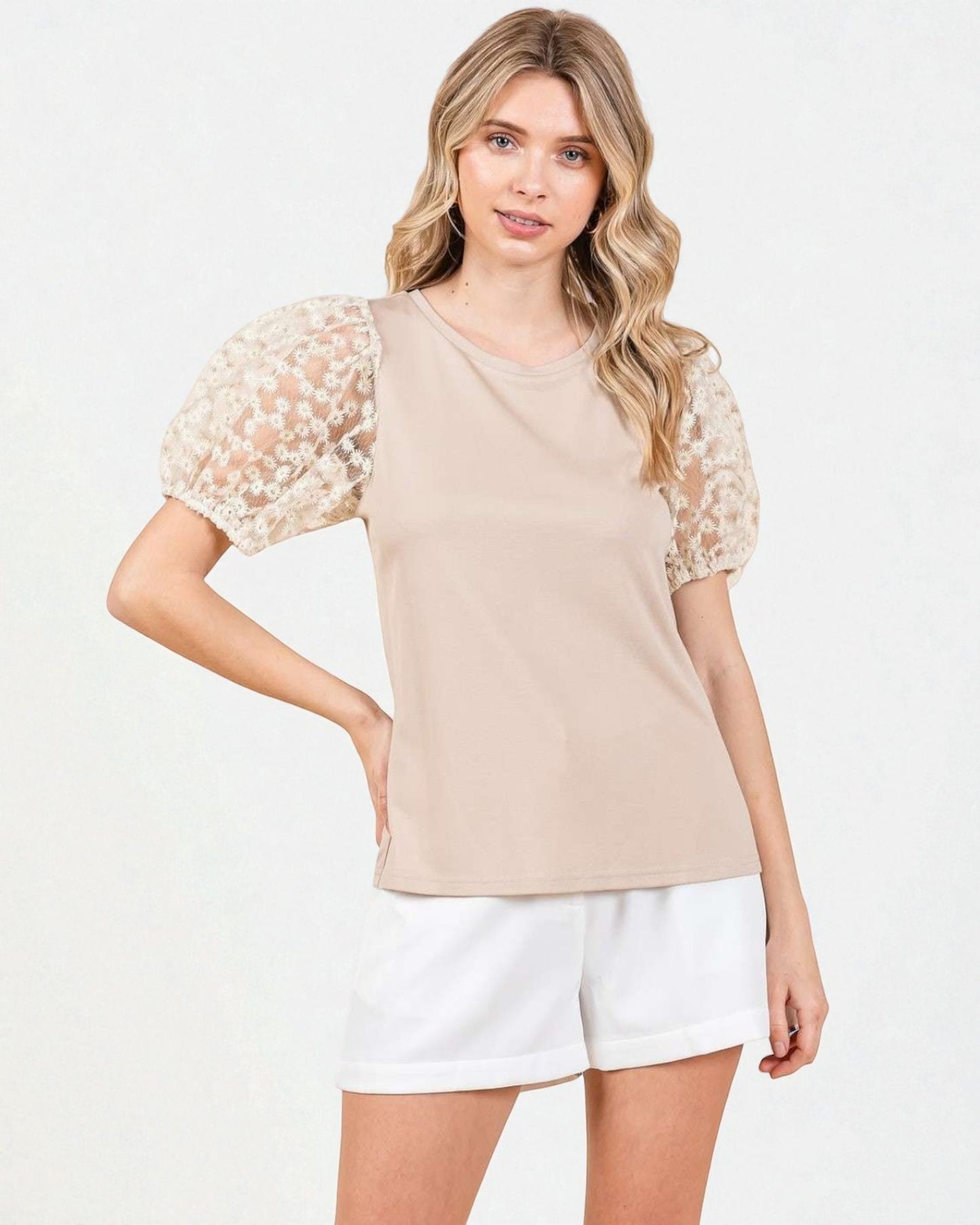 Woman wearing a beige top with floral sleeves and white shorts on a light background