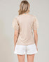 Woman wearing a beige top with floral sleeves and white shorts on a plain background