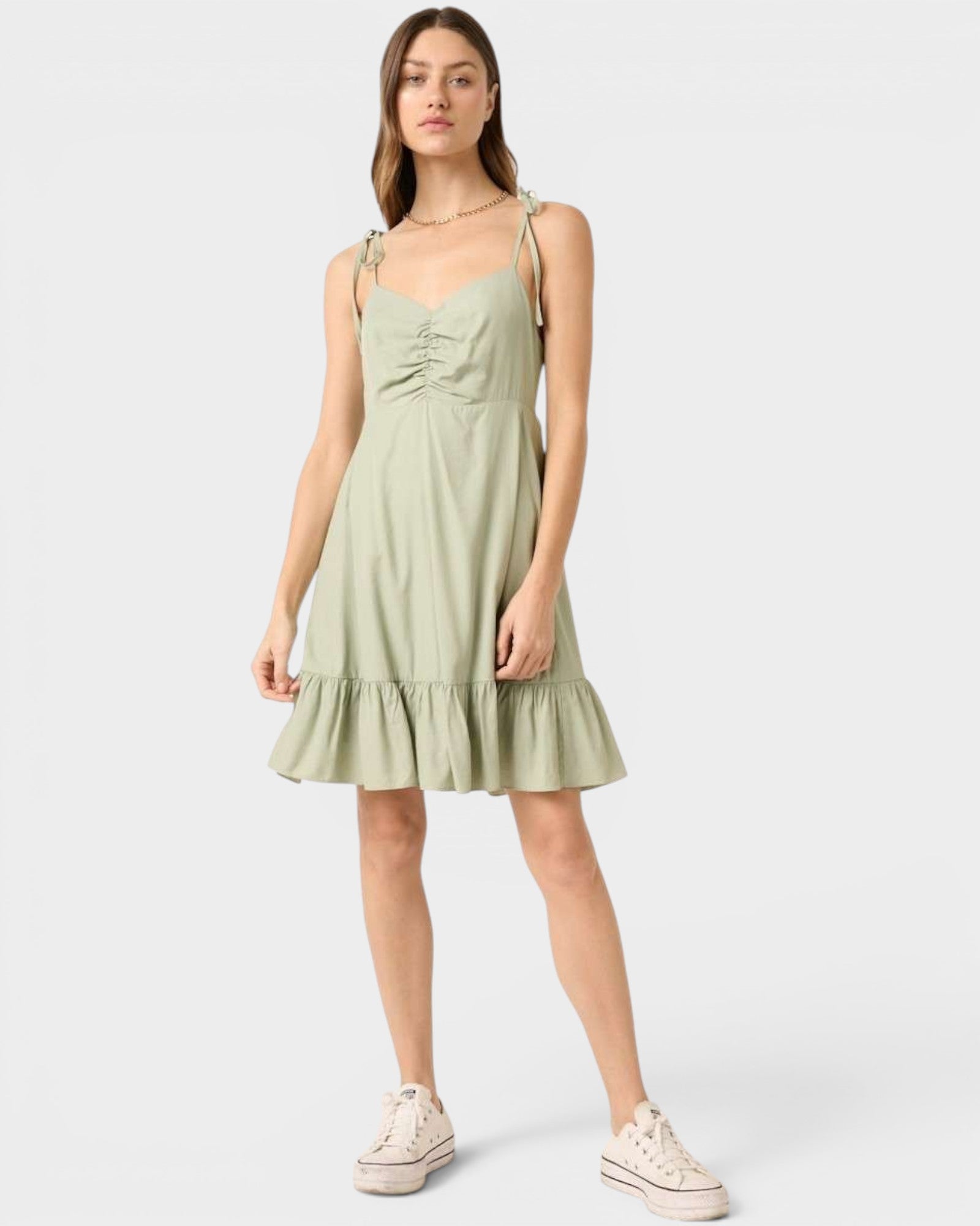 Woman wearing a light green dress with ruched bodice and tiered skirt on a white background