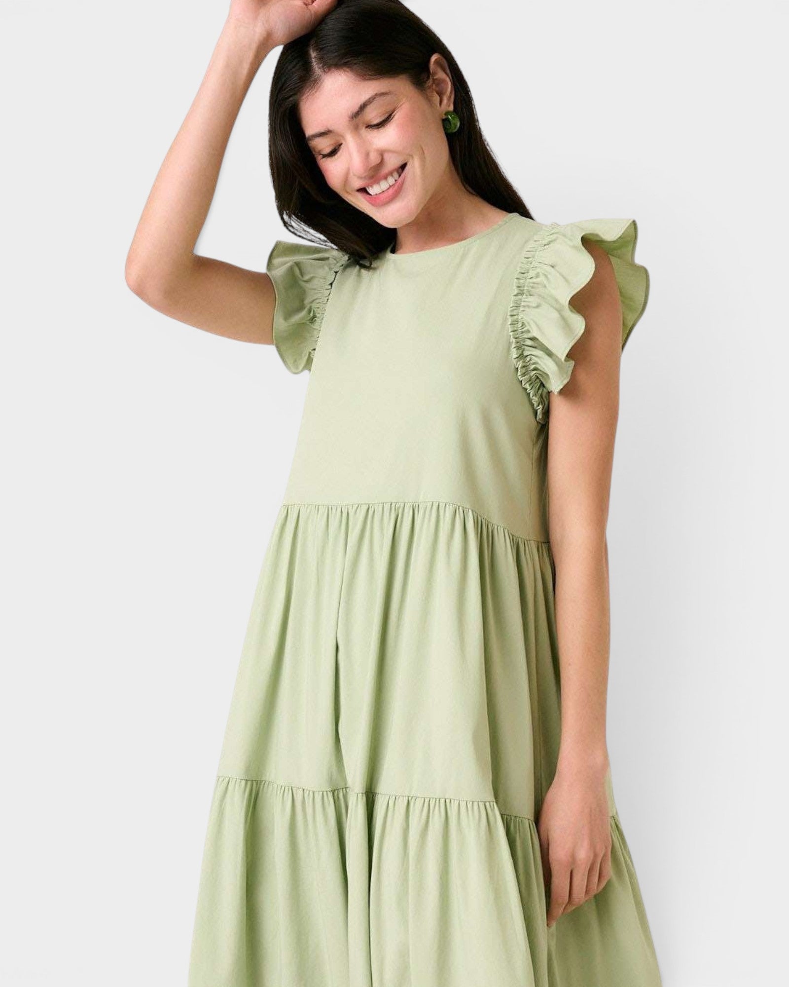 Woman wearing a light green dress with ruffled sleeves against a white background