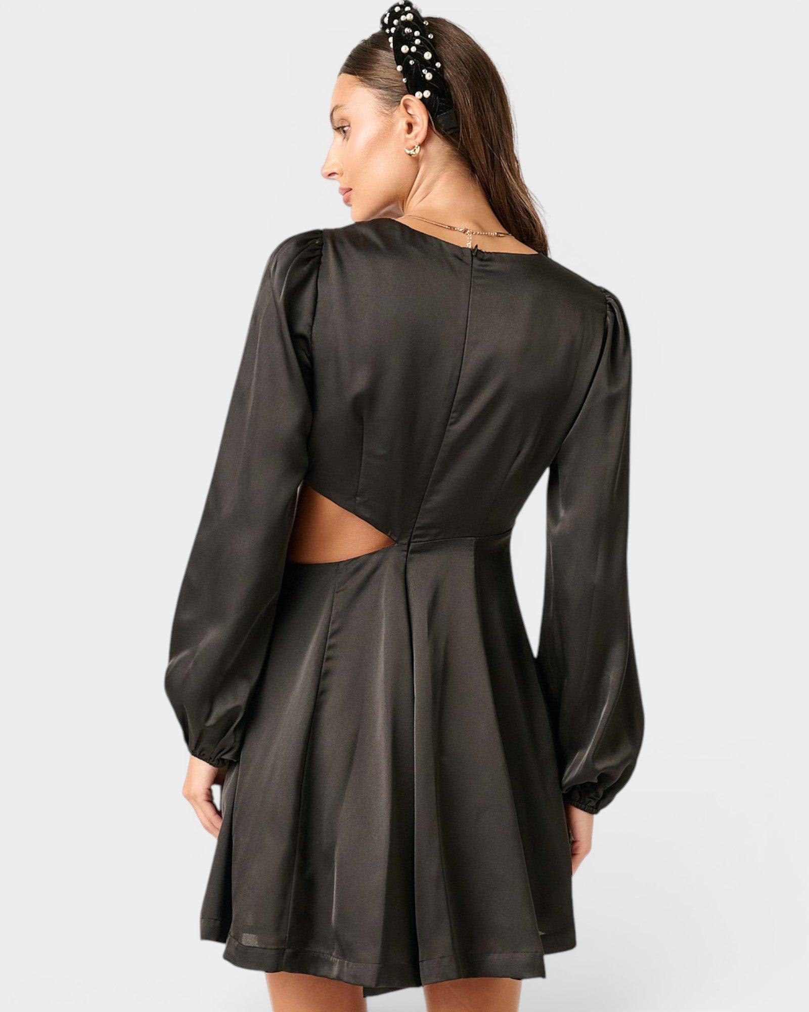Woman wearing a black dress with long sleeves and cut-out back on a white background