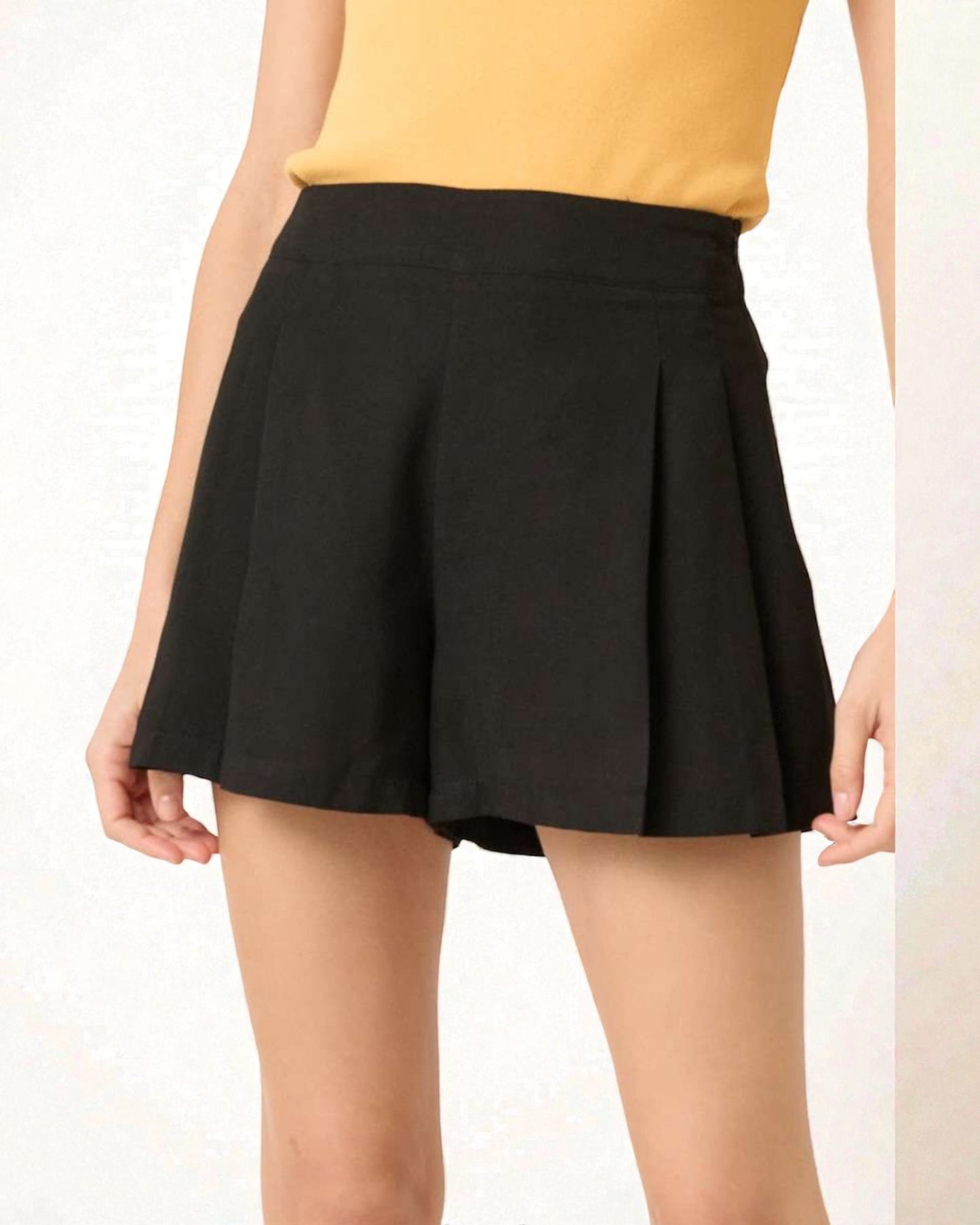 Black pleated shorts worn by a person on a white background