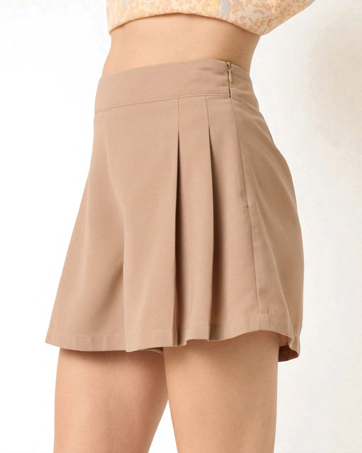 Beige pleated shorts worn by a person on a white background