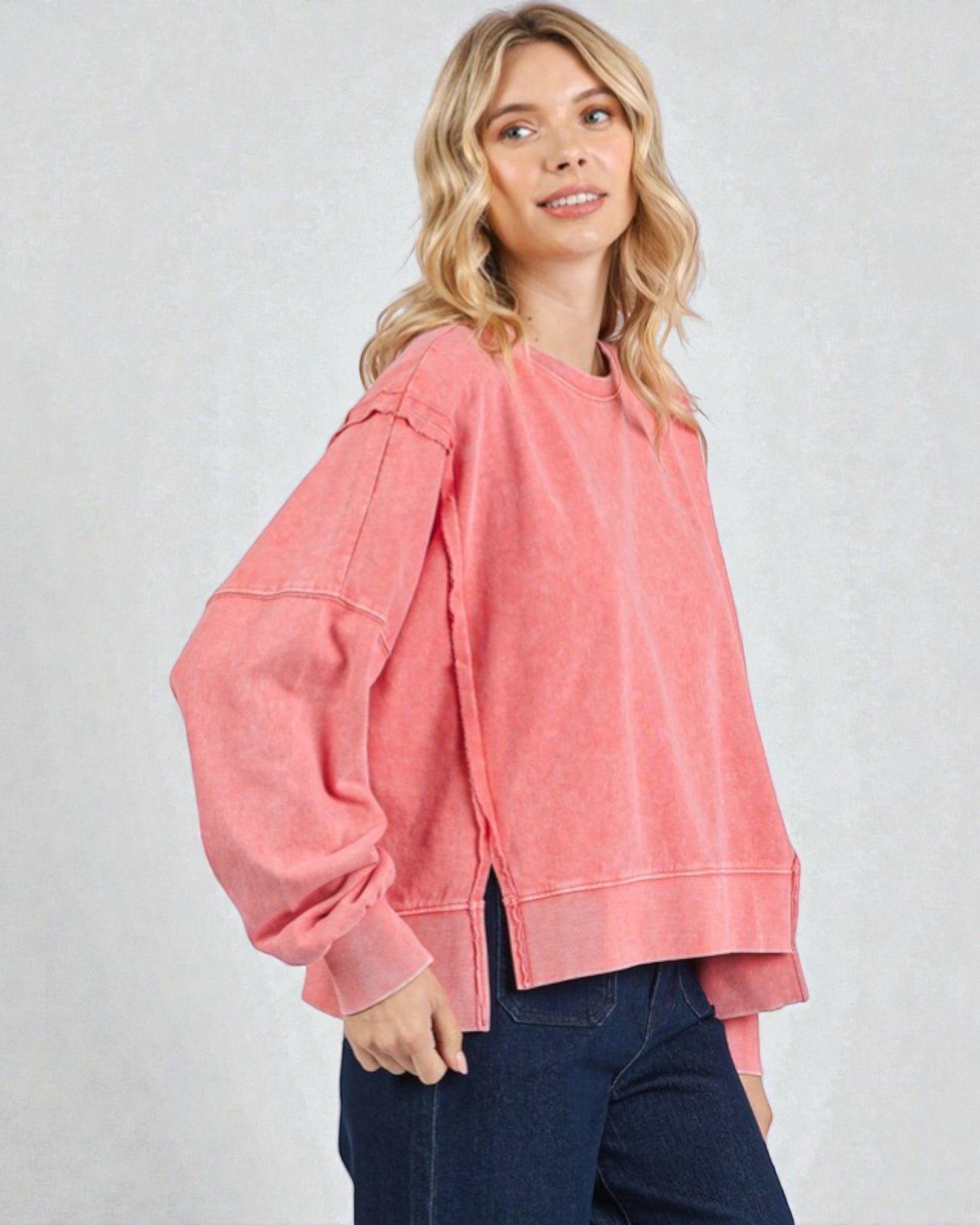 Woman wearing a pink sweatshirt and blue jeans on a gray background