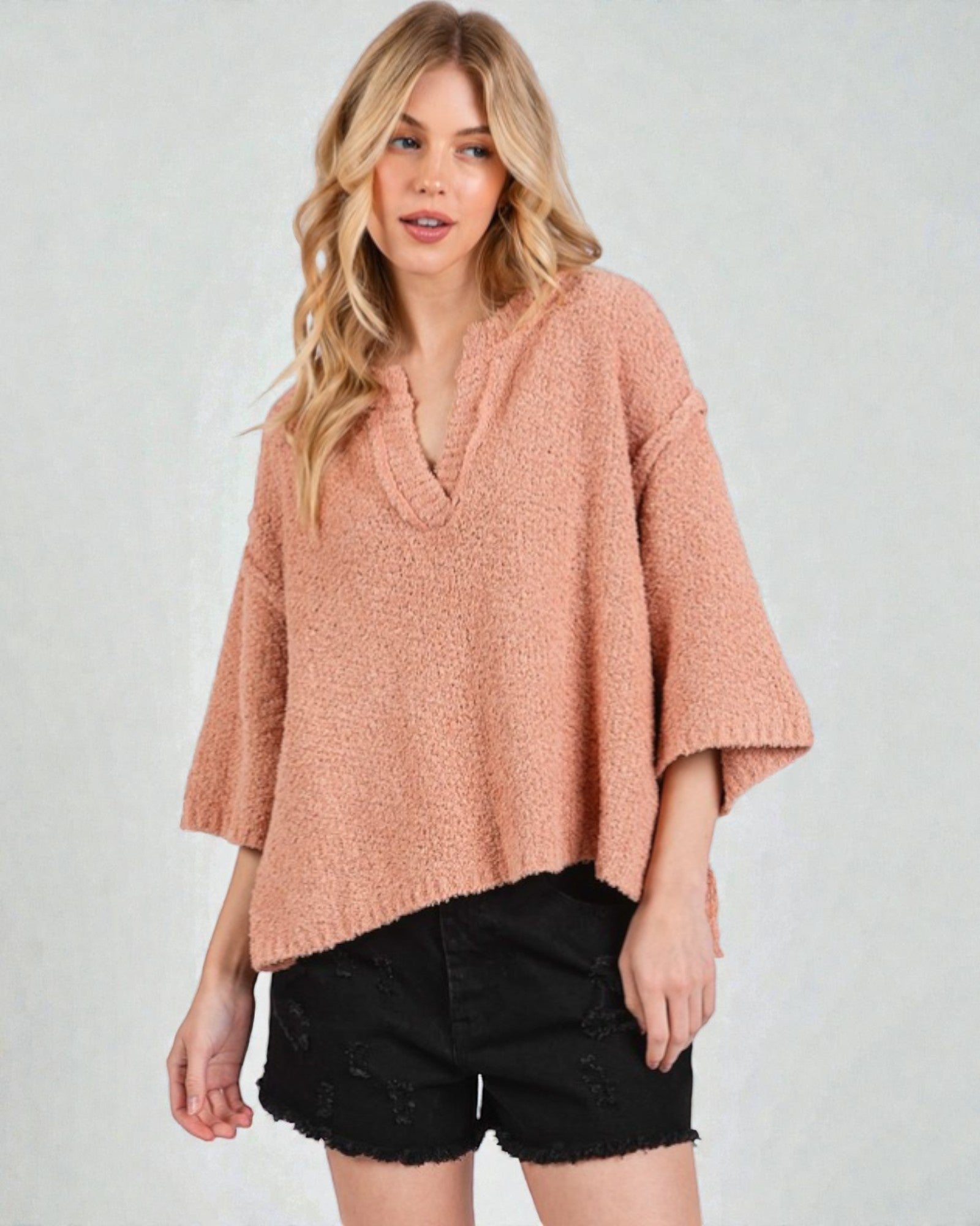 Woman wearing a pink poncho over a black top on a white background