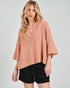 Woman wearing a pink poncho over a black top on a white background