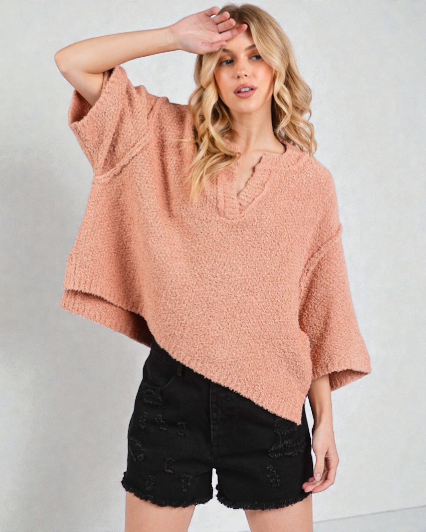 Woman wearing a pink oversized sweater and black shorts on a white background