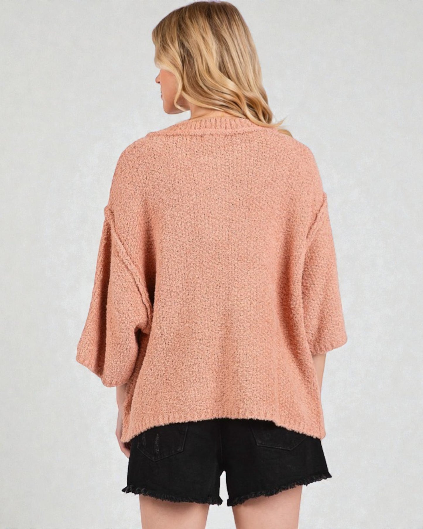 Woman wearing a pink sweater and black shorts on a plain background