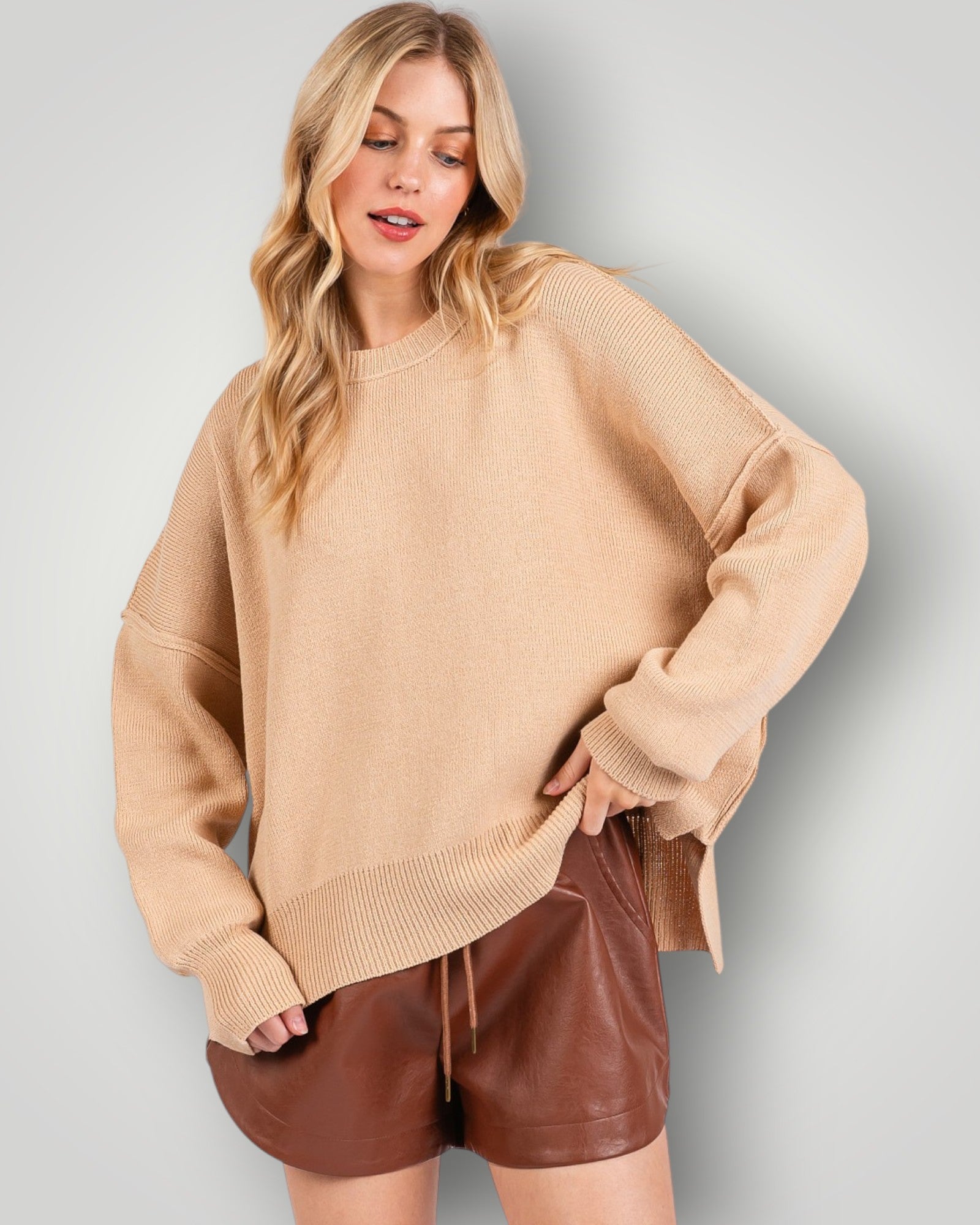 Woman wearing a beige sweater and brown shorts against a light gray background