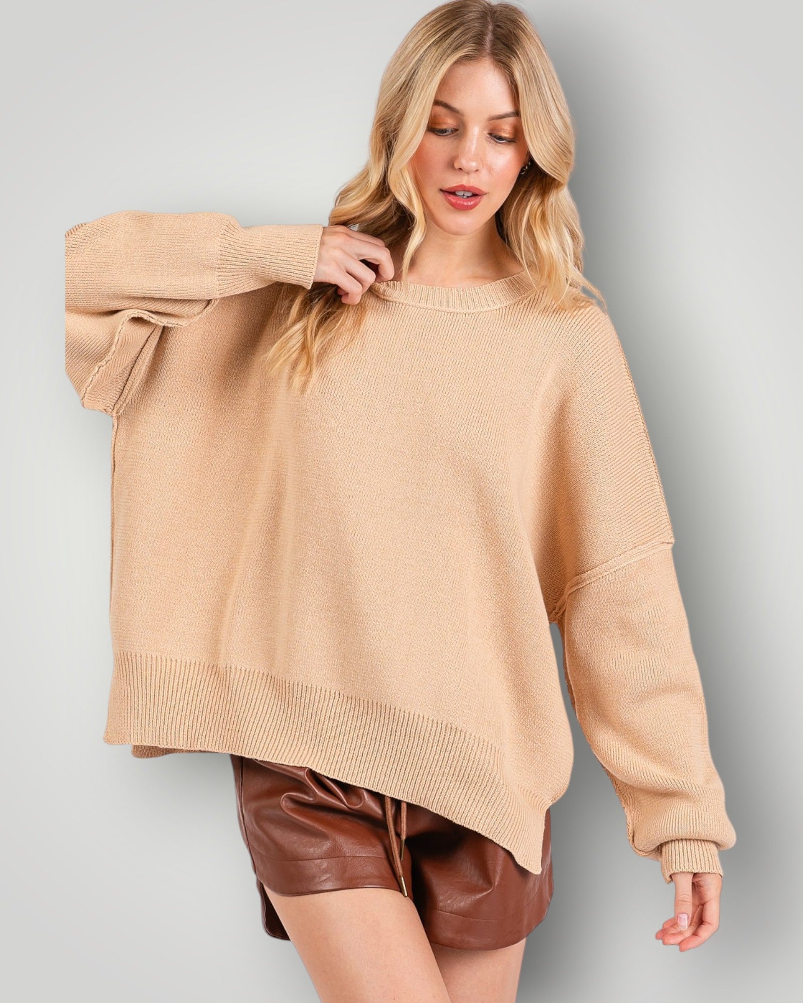 Woman wearing a beige sweater and brown shorts on a gray background