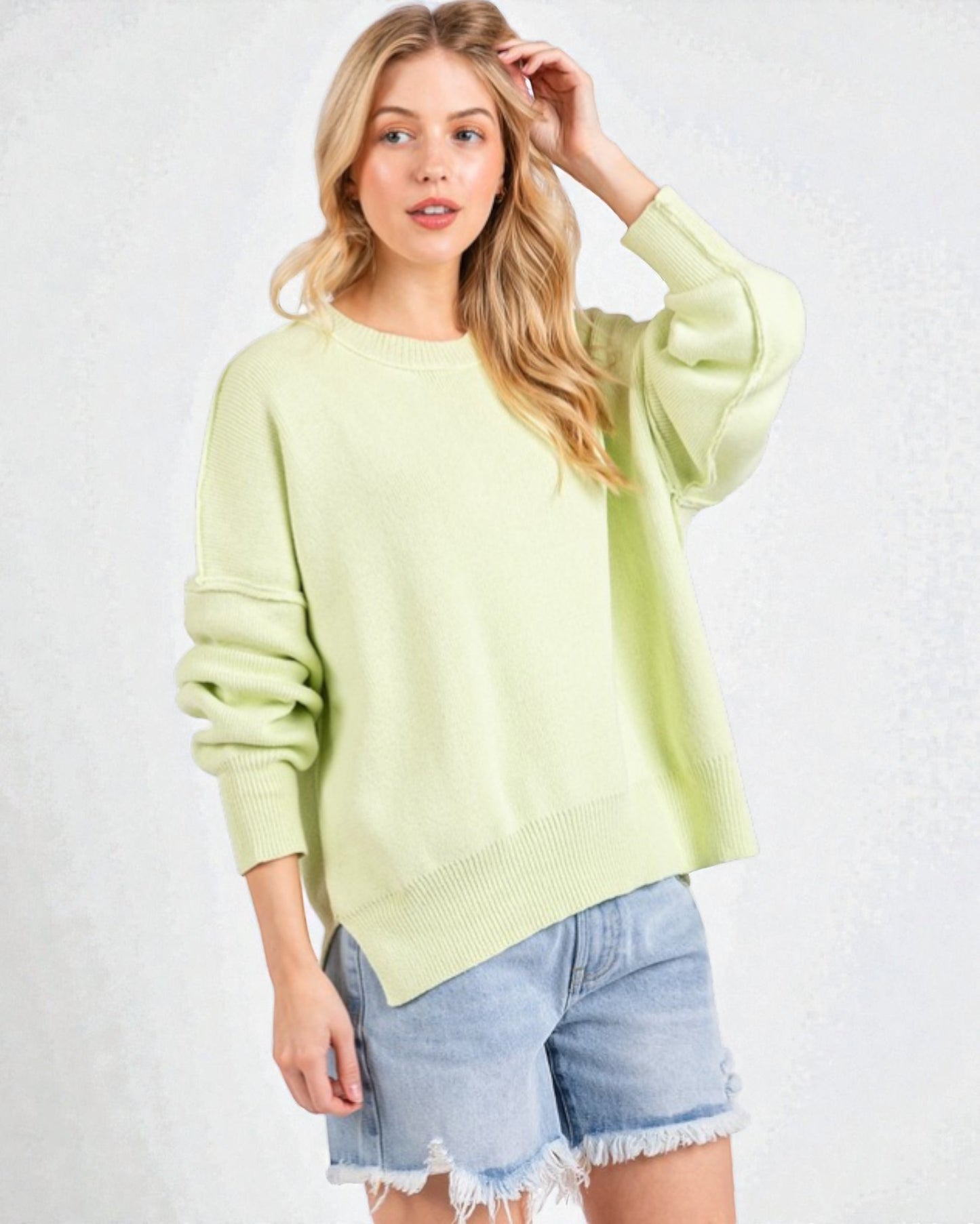 Woman wearing a light green sweater and denim shorts on a white background