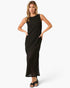 A woman modeling a sleeveless black maxi dress with a textured, open-knit pattern and side pockets, paired with black slide sandals, against a plain white studio background.