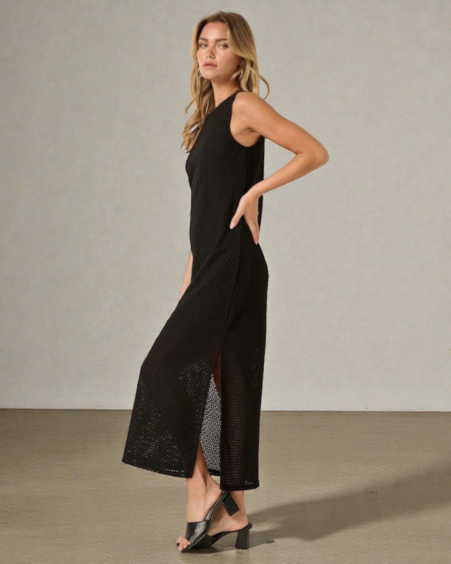 Woman wearing a black sleeveless dress with a slit on a plain background