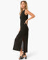 A woman modeling a sleeveless black maxi dress with a textured, open-knit pattern and a high side slit, paired with black heeled sandals against a plain white studio background.