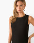 A woman wearing a sleeveless black textured knit top with a crew neckline, photographed against a clean white studio background.