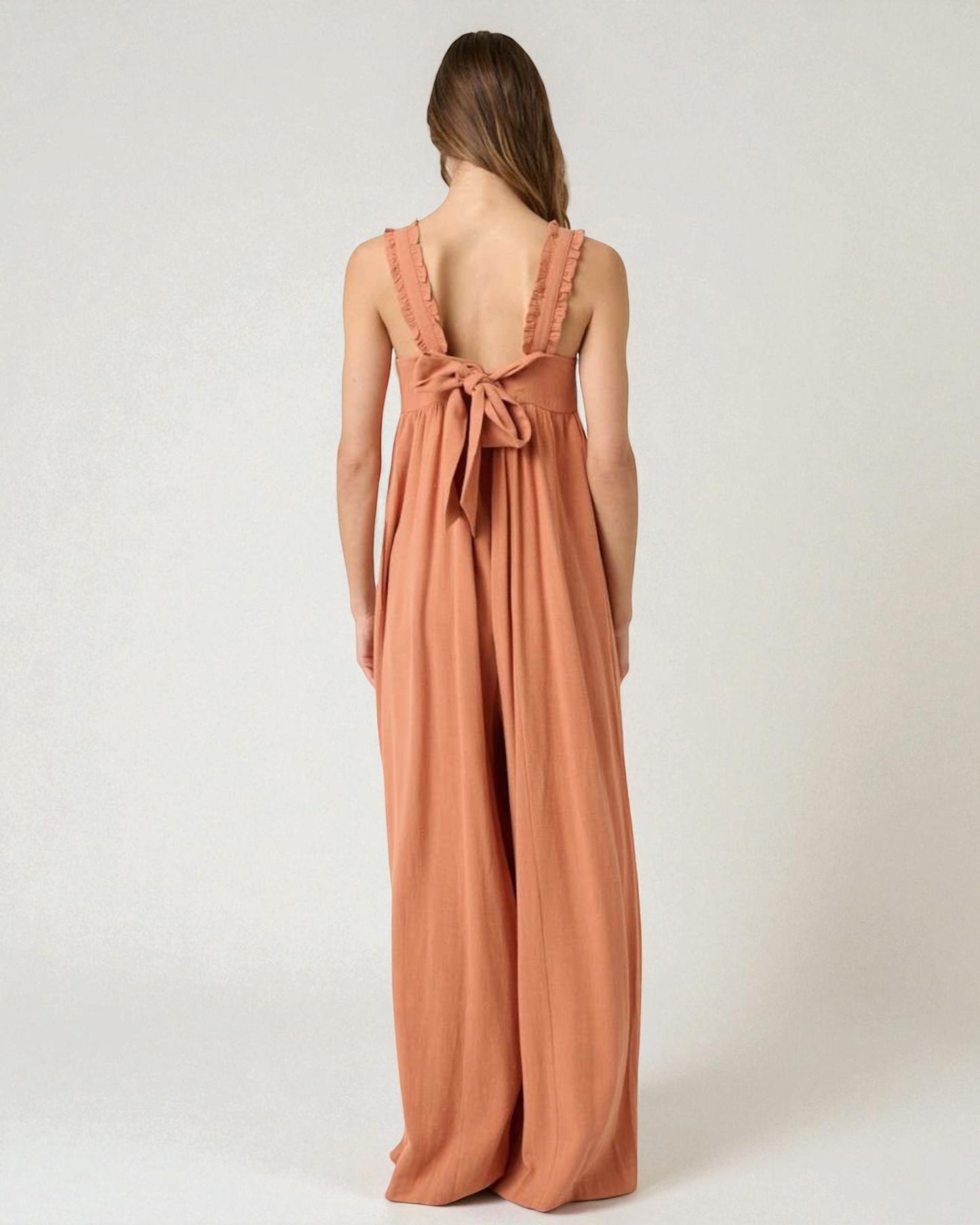 Woman wearing a long, flowing dress with a bow detail on a plain background