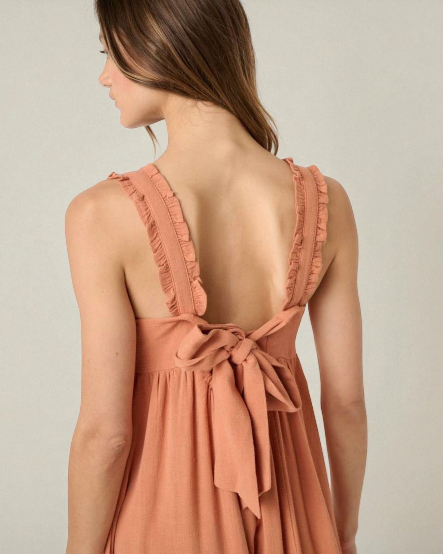 Woman wearing a peach-colored dress with a bow detail on a plain background