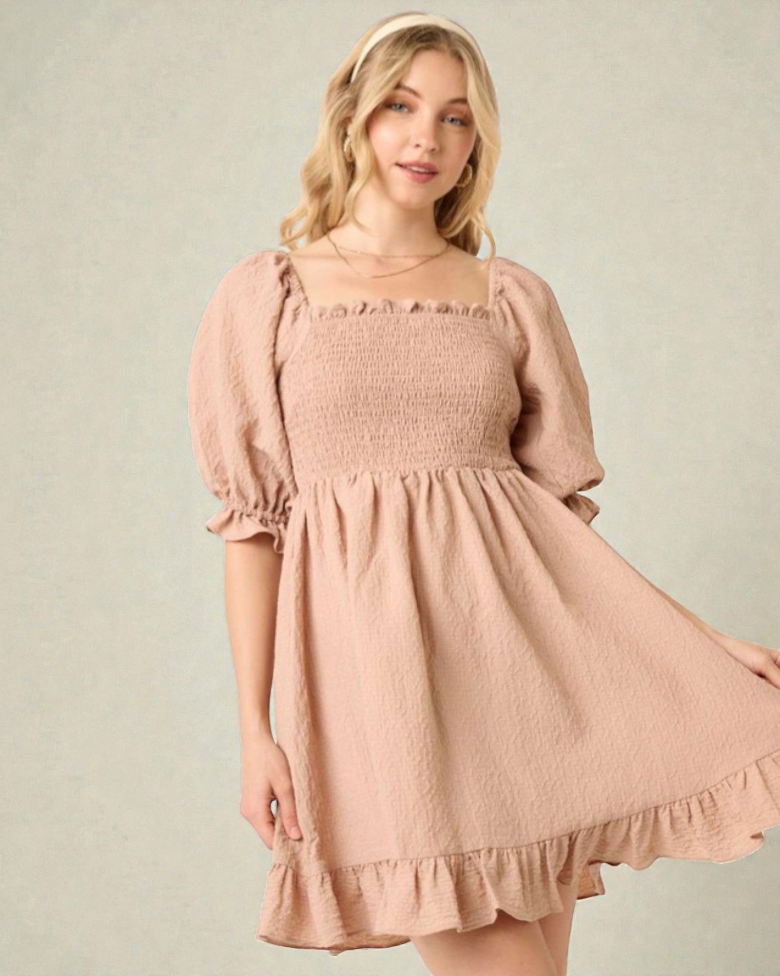 Woman wearing a pink smocked dress with puffed sleeves on a plain background