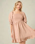 Woman wearing a pink smocked dress with puffed sleeves on a plain background