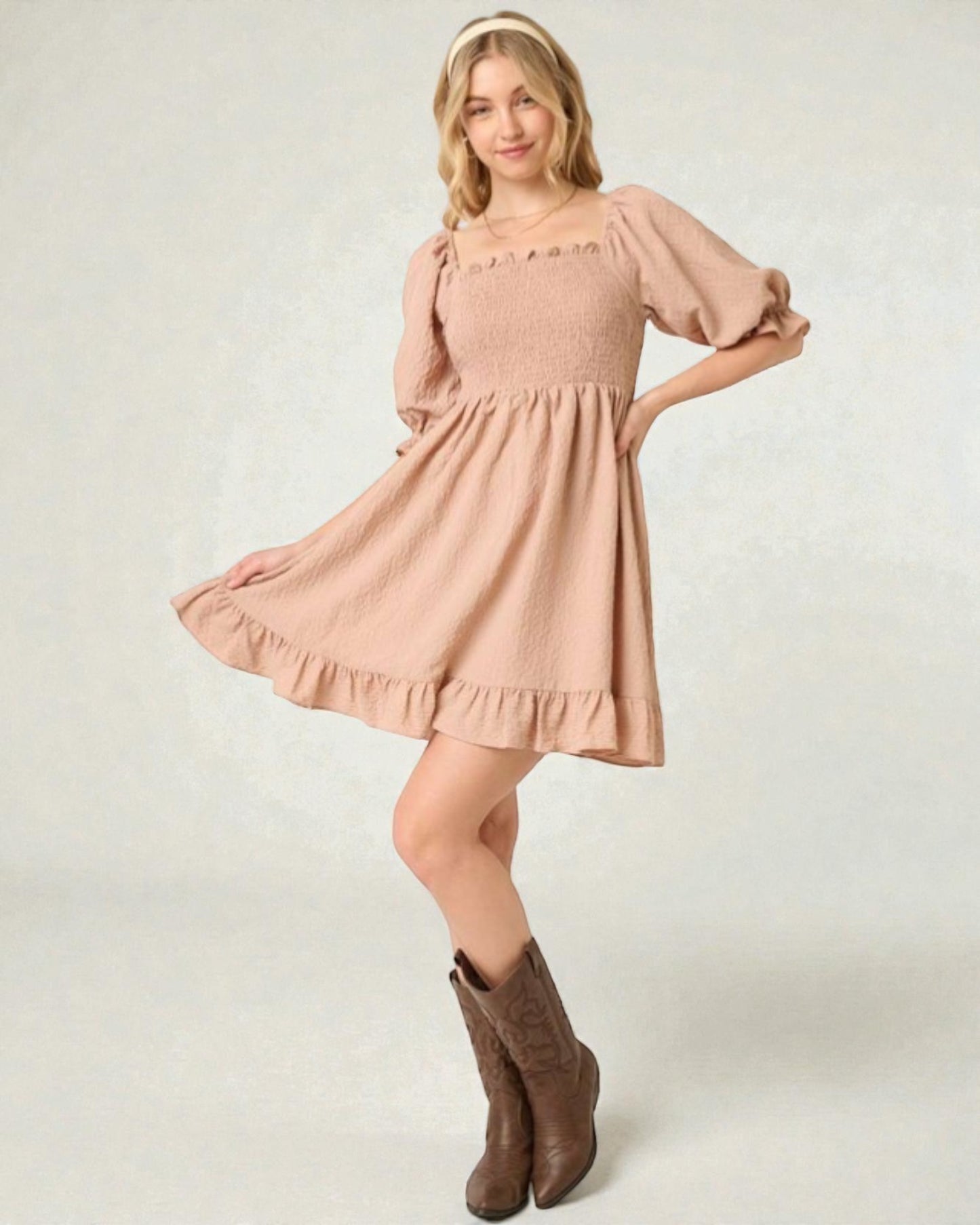 Woman wearing a pink dress with ruffled sleeves and hem, standing against a plain background.