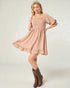 Woman wearing a pink dress with ruffled sleeves and hem, standing against a plain background.