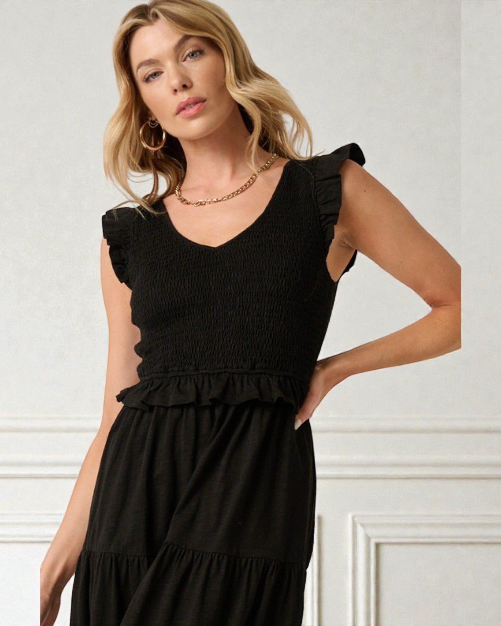 Woman wearing a black sleeveless dress with ruffled details against a white background