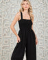 Woman wearing a black jumpsuit against an intricate wall pattern