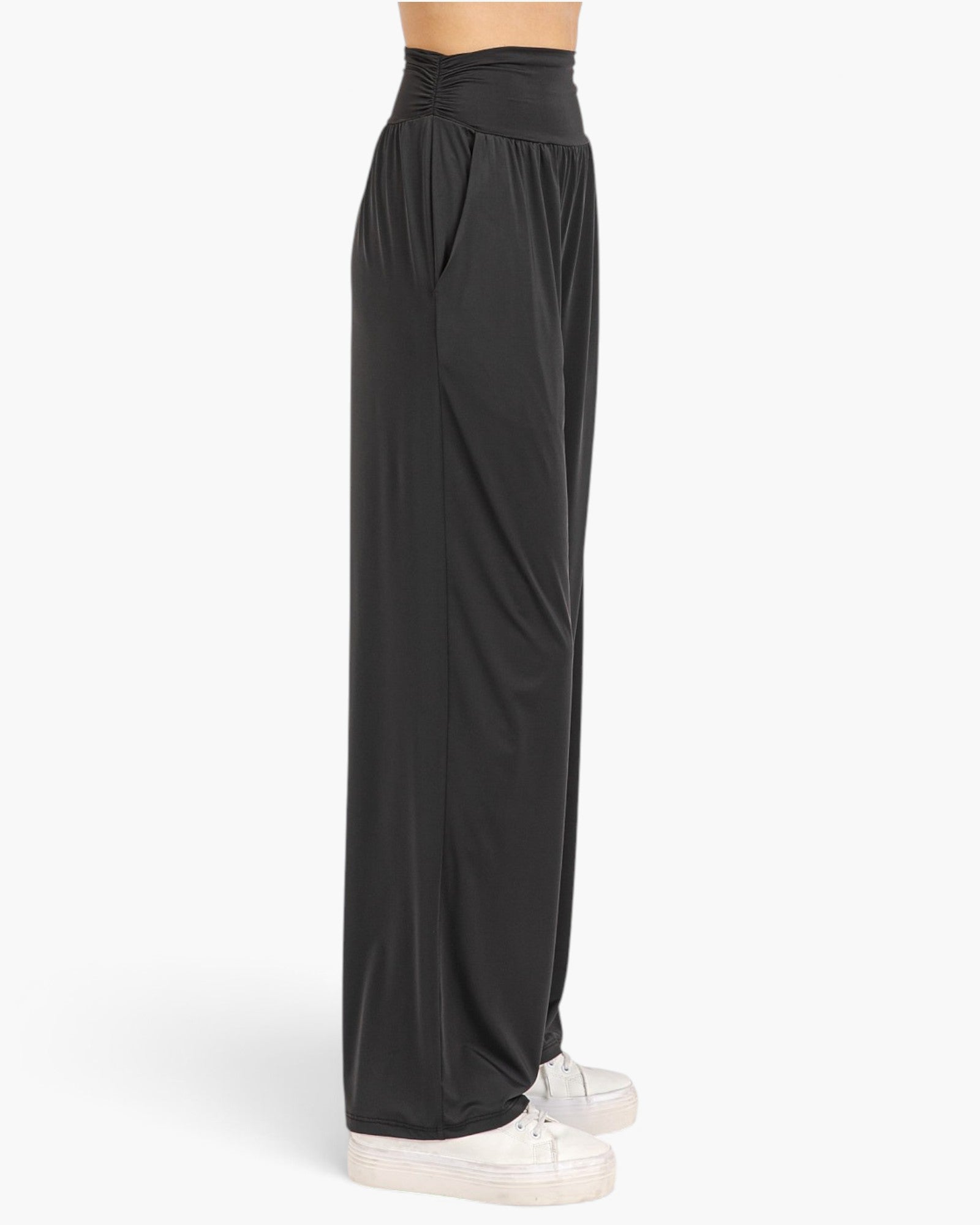 Black wide-leg lounge pants with a gathered elastic waistband, shown on a model from the waist down wearing white sneakers against a light gray background.