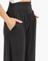 Close-up of a person wearing black wide-leg pants with a gathered elastic waistband and side pockets, shown against a plain light background.