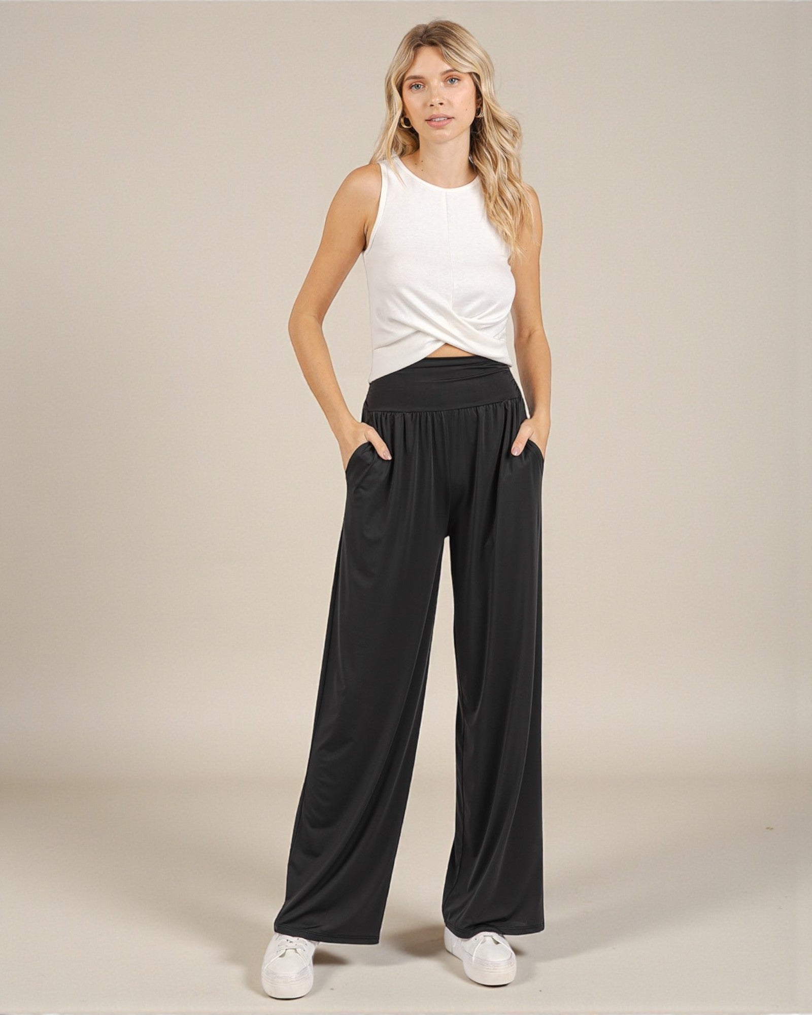 Woman wearing a white sleeveless top and black wide-leg pants on a beige background