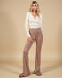 Woman wearing a white sweater and brown flared pants on a beige background