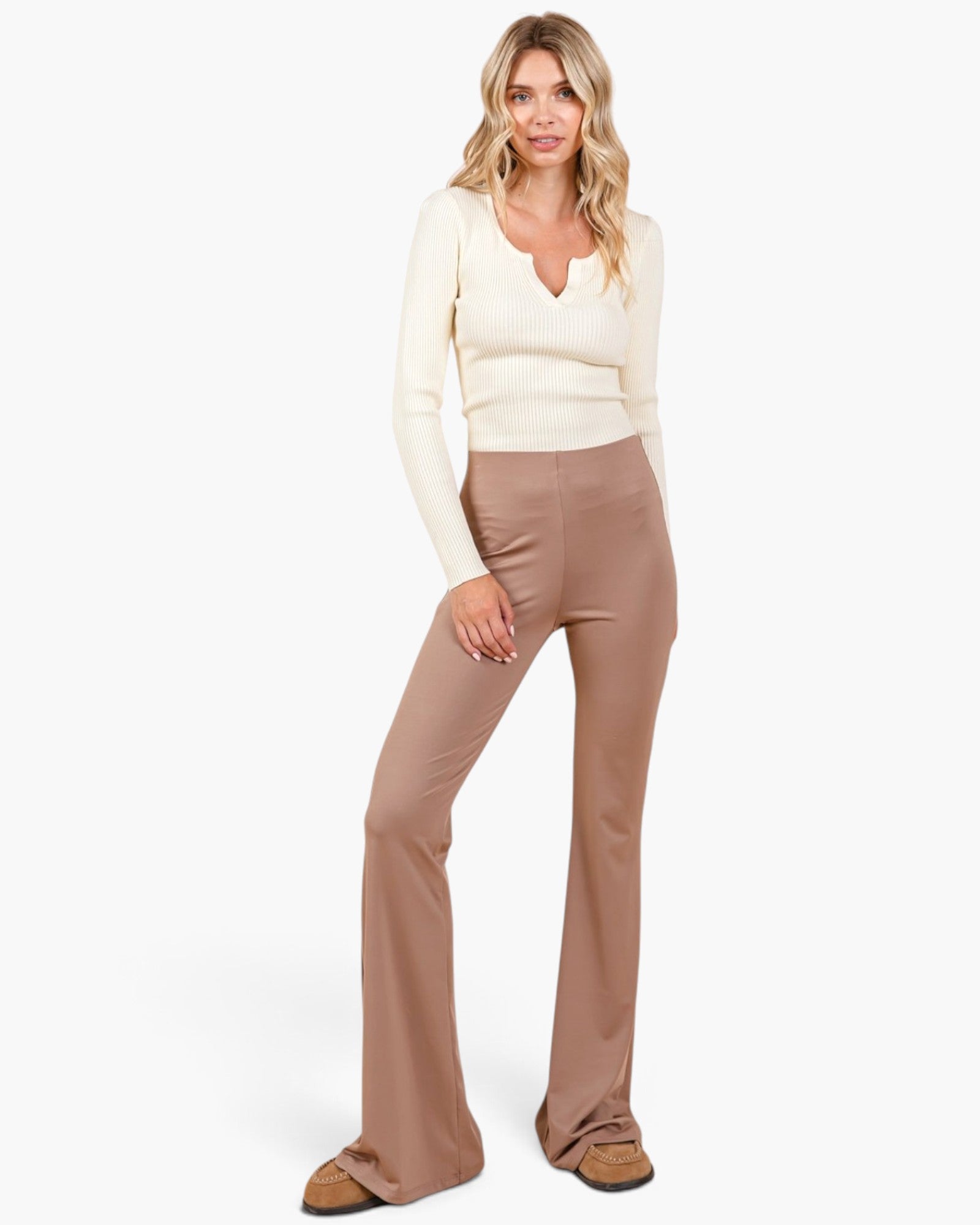 A woman modeling a cream long-sleeve knit top and high-waisted, straight-leg taupe pants against a plain white studio background.