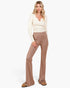 A woman modeling a cream long-sleeve knit top and high-waisted, straight-leg taupe pants against a plain white studio background.