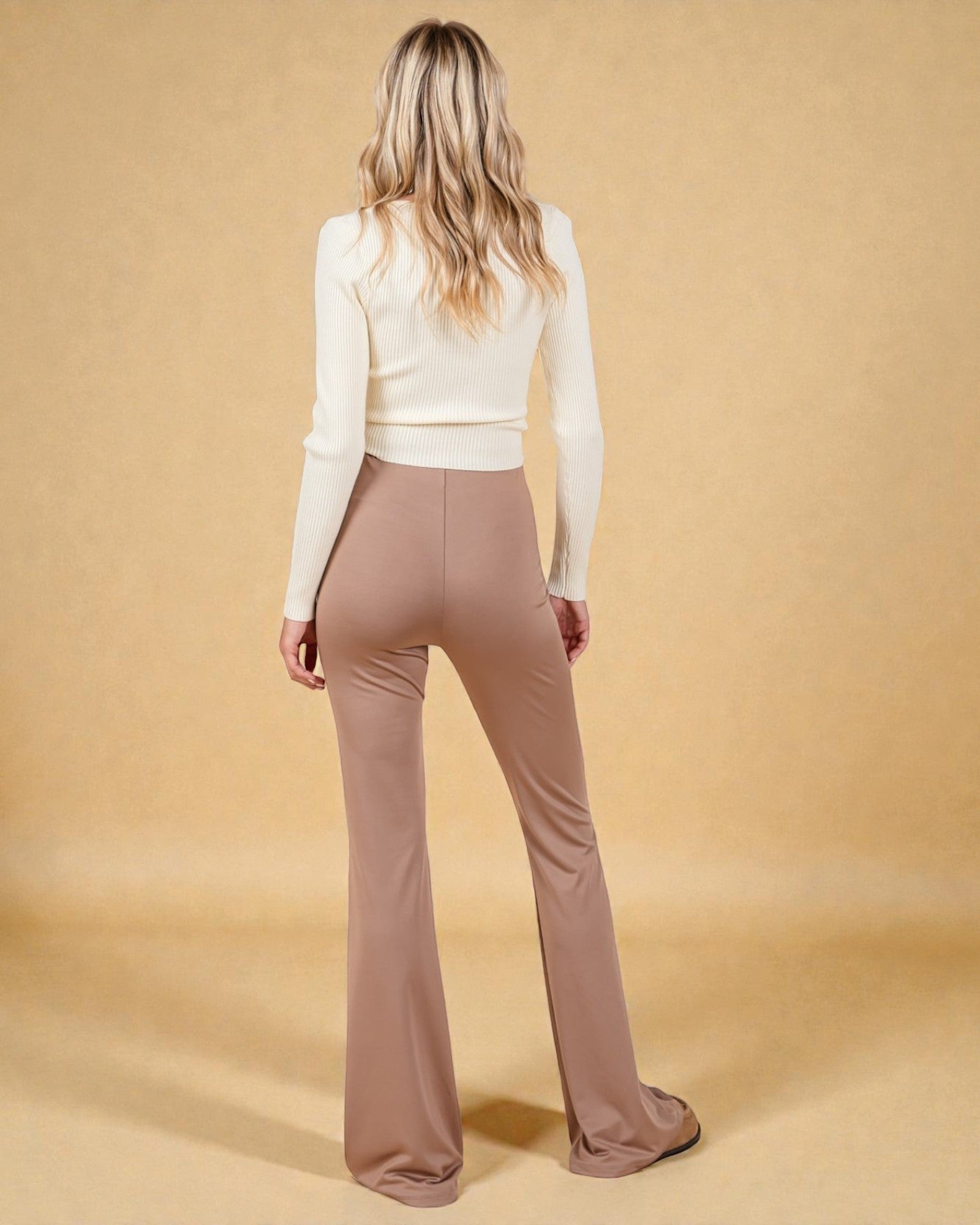Woman wearing a white top and brown flared pants on a beige background