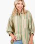 A smiling blonde woman wearing a loose button-up shirt with vertical stripes in sage green, olive, and beige, paired with light blue jeans, against a plain white background.