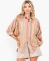 A woman modeling a loose, short-sleeve button-up shirt with vertical stripes in pink, yellow, green, and beige, paired with beige shorts against a plain white background.