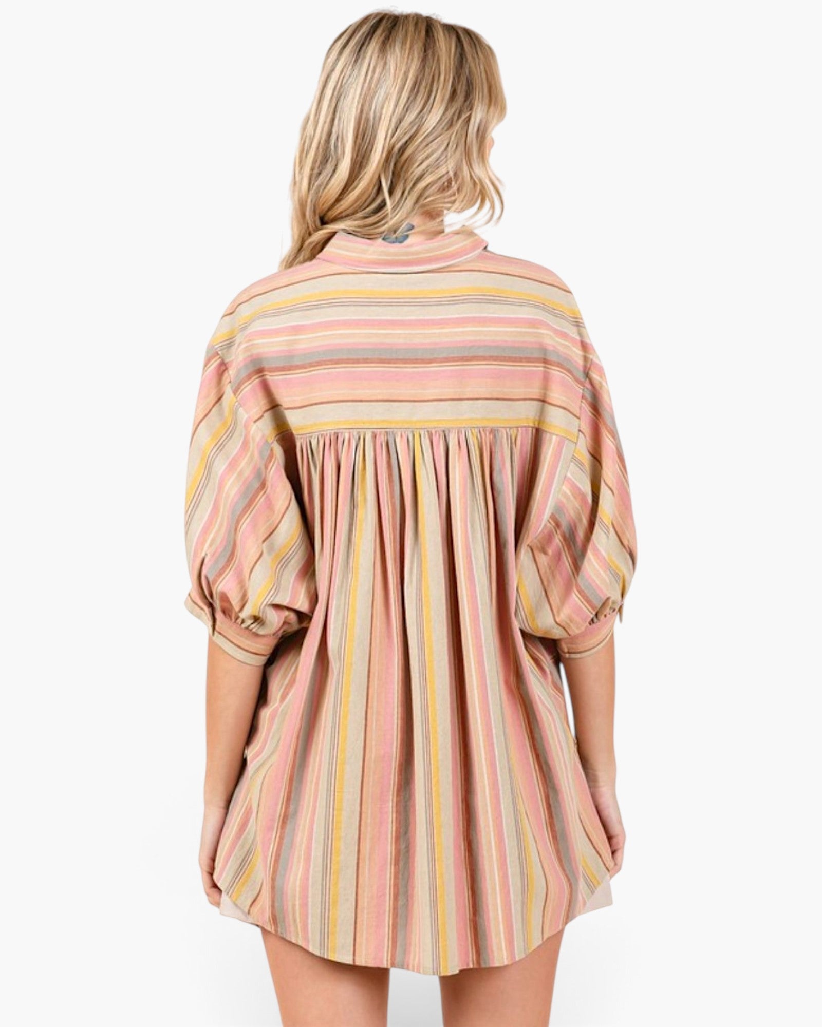 A woman viewed from the back wearing a loose, short-sleeve striped dress with vertical bands in dusty pink, yellow, beige, and light blue on a plain white background.