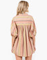 A woman viewed from the back wearing a loose, short-sleeve striped dress with vertical bands in dusty pink, yellow, beige, and light blue on a plain white background.