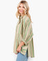 A woman wearing a loose, oversized striped button-up shirt in beige, green, and brown tones, paired with light blue jeans, photographed against a clean white studio background.