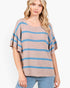A woman wearing a loose, short-sleeve knit top with horizontal blue stripes on a taupe background, paired with light blue jeans, against a plain white studio background.