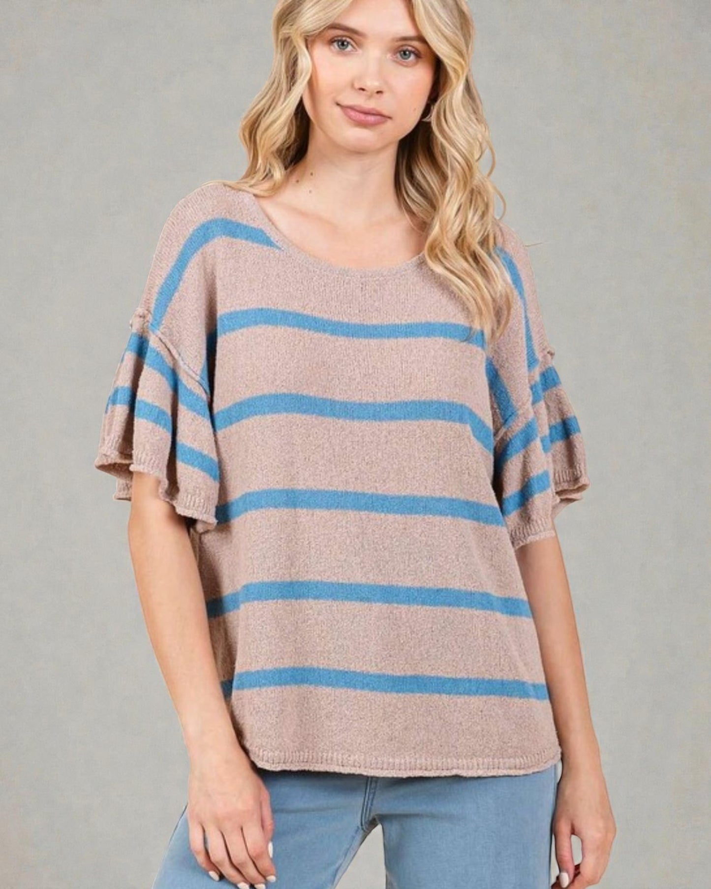 Woman wearing a striped sweater with bell sleeves against a gray background