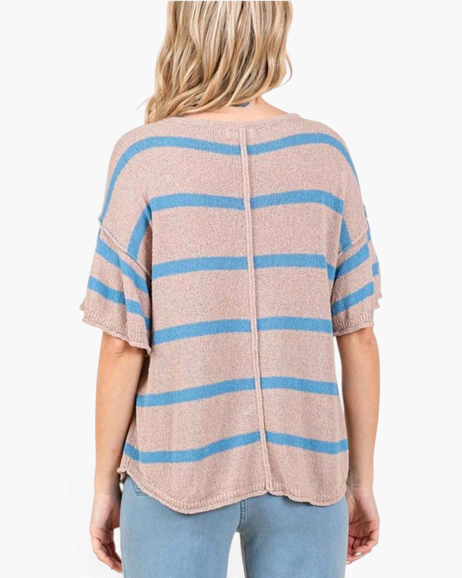 A woman shown from the back wearing a loose, short-sleeve knit top with horizontal light blue stripes on a heathered beige-pink base, paired with light blue jeans against a plain white background.