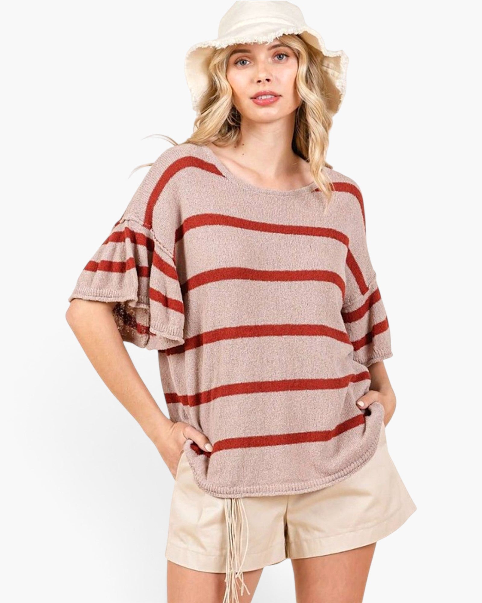 A woman wearing a beige knit top with horizontal rust-red stripes, paired with beige shorts and a cream bucket hat, against a plain white background.