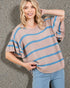Woman wearing a beige and blue striped sweater against a textured wall.