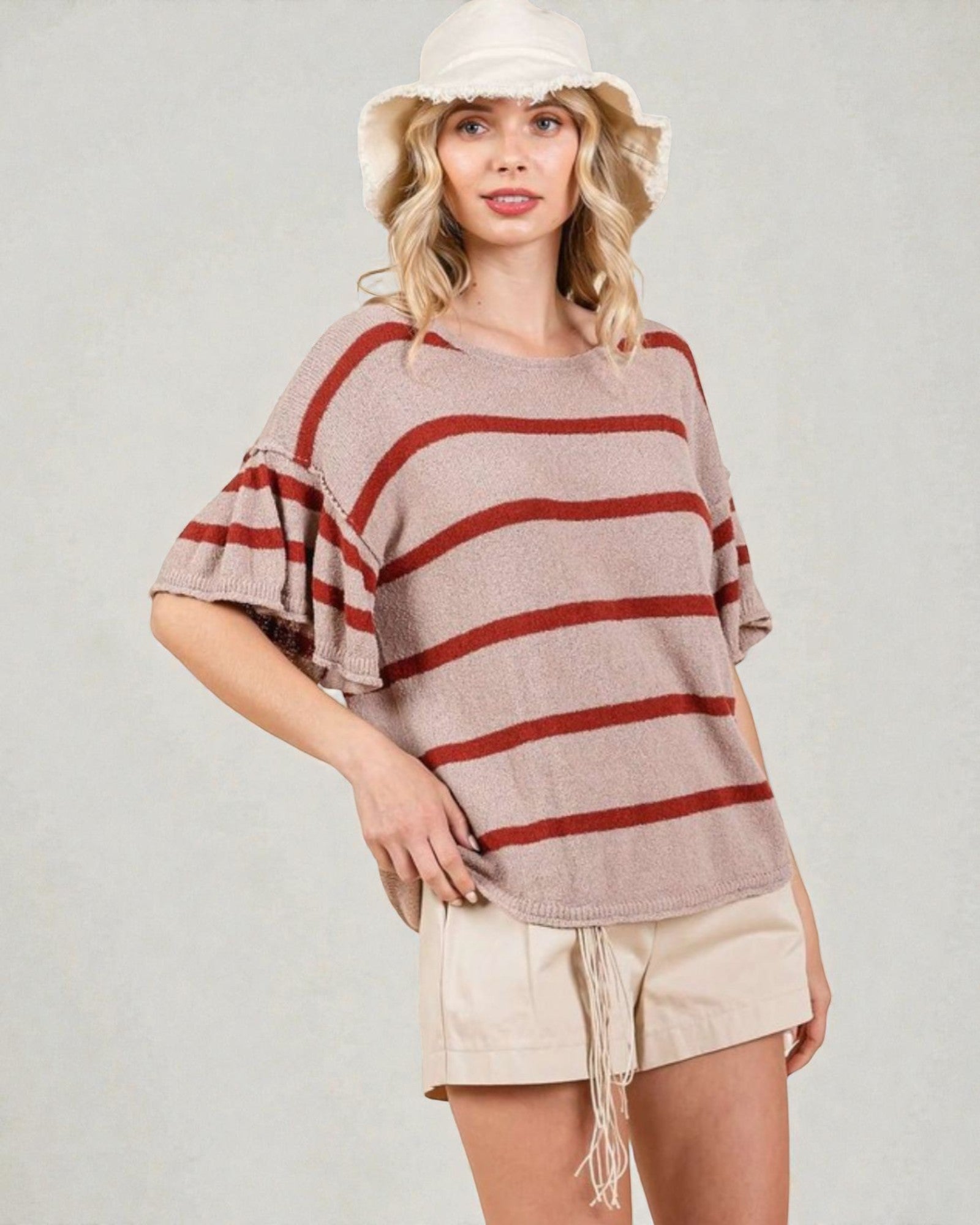 Woman wearing a striped sweater and shorts with a white hat on a plain background