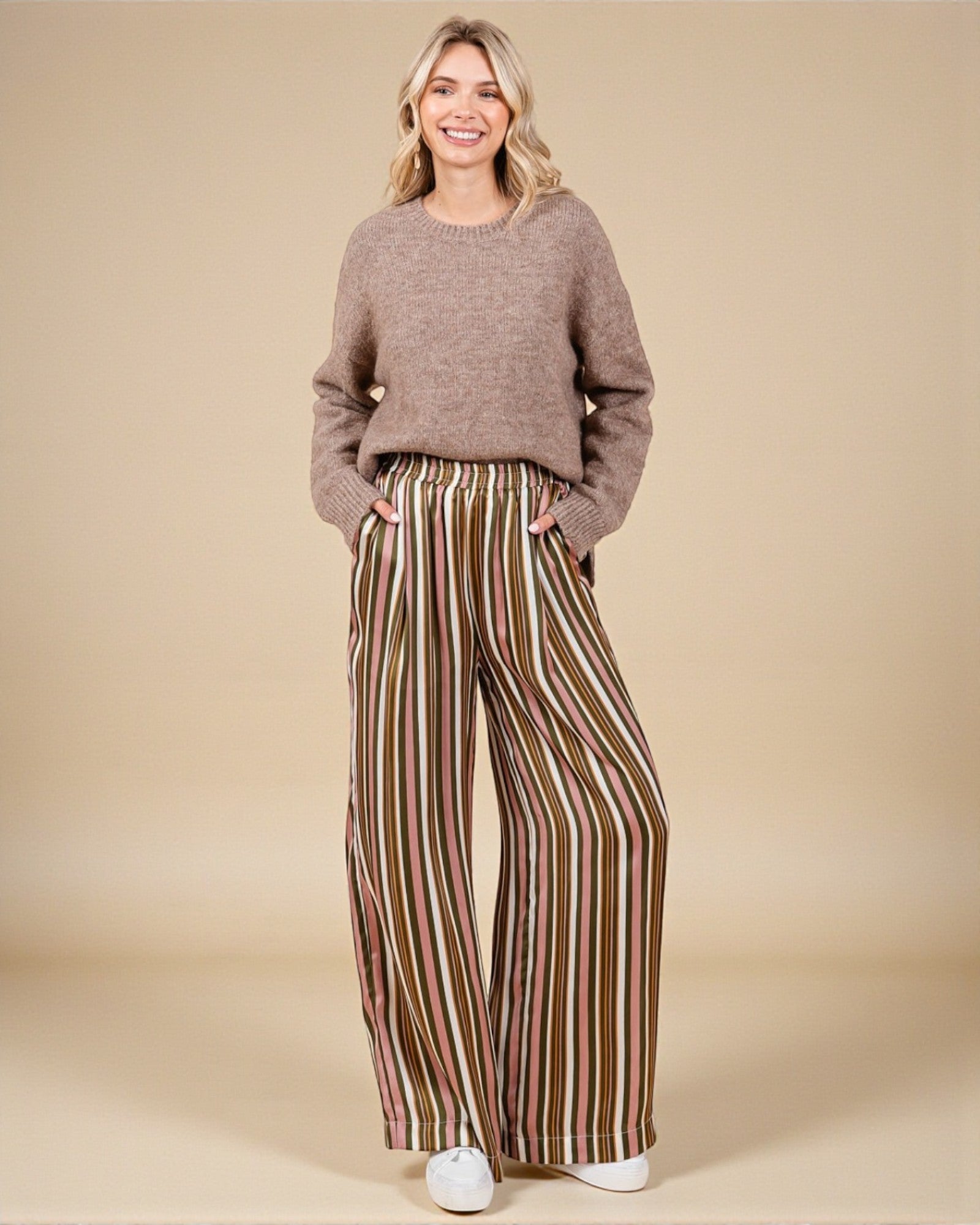 Woman wearing a brown sweater and striped pants on a beige background