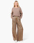 A woman modeling a cozy taupe knit sweater and wide-leg striped trousers with vertical stripes in brown, gold, and cream, standing against a plain white studio background.