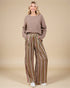 Woman wearing a brown sweater and striped pants on a beige background